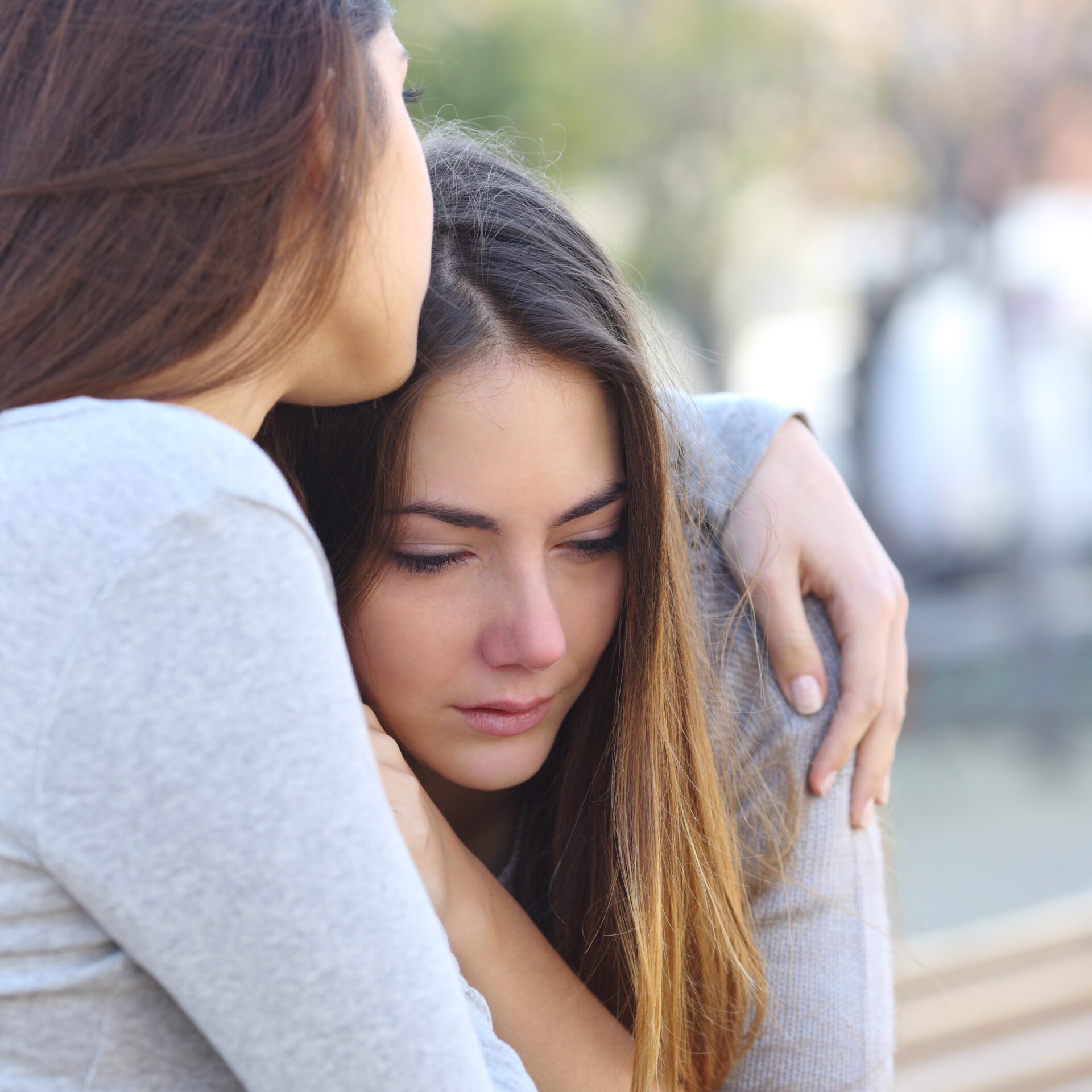 Sad girl crying and a friend comforting her outdoors in a park